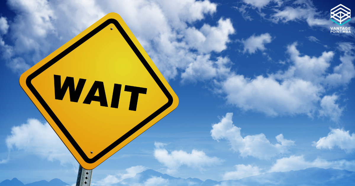 Yellow road sign with the word 'WAIT' against a blue sky with clouds, representing the concept of being on an MBA waitlist.